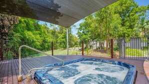 Ein Whirlpool auf einer Holzterrasse mit Metallgeländer, umgeben von Bäumen und einem Zaun.