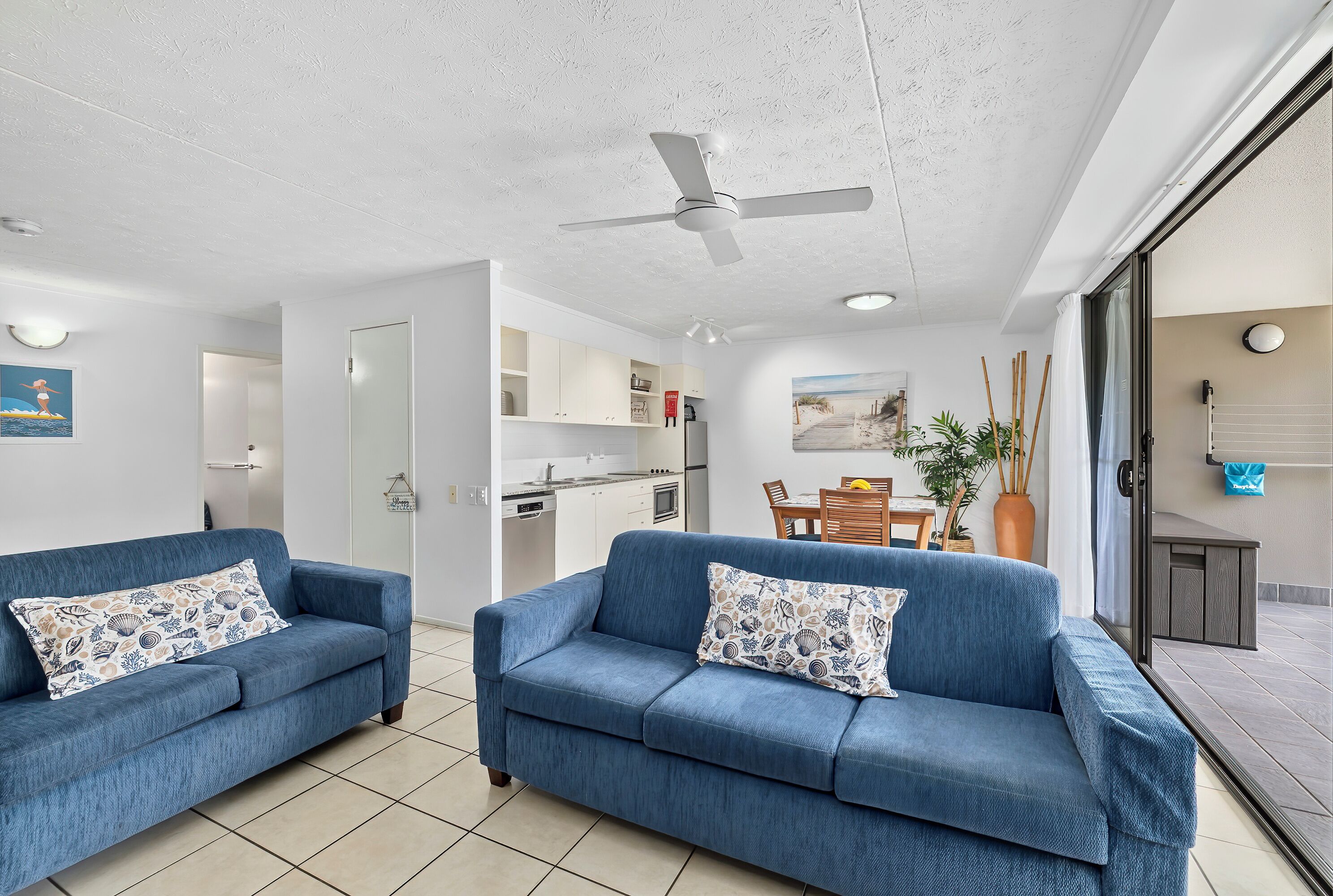 Ein modernes Wohnzimmer mit zwei blauen Sofas, einem Deckenventilator und Blick auf eine Küche und einen Essbereich.
