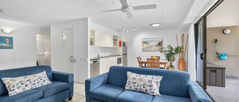 Ein modernes Wohnzimmer mit zwei blauen Sofas, einem Deckenventilator und Blick auf eine Küche und einen Essbereich.