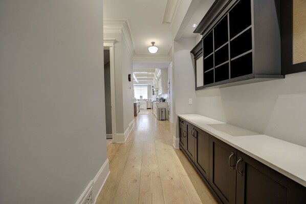 A hallway with a wooden floor, white walls, and a kitchen area in the distance.