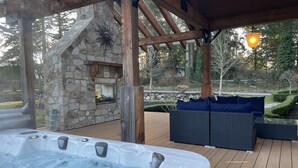 A hot tub in a covered outdoor area with stone walls, wooden beams, and a stone fireplace. - 9 bdrm home, sleeps 26 w/ hot tub/gym/theatre/bar (Surrey)