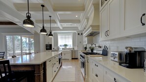 A modern kitchen with white cabinetry, a central island, pendant lighting, and a view of the outdoors through large windows. - 9 bdrm home, sleeps 26 w/ hot tub/gym/theatre/bar (Surrey)
