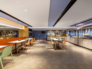 A modern restaurant interior with tables and chairs, a counter with a display case, and a blue wall with signage. - Hanting Hotel (Beijing)