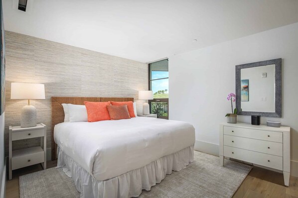 A bedroom with a large bed, nightstands, a dresser, a mirror, and a view of the outdoors.