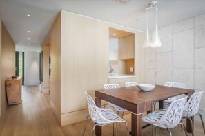 A modern dining area with a wooden table and white chairs, a white bowl on the table, and pendant lights above. - Hapuna Beach Residences C43 (KAMUELA)