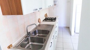 Une cuisine équipée d’un évier à deux bacs, d’une cuisinière à gaz et de meubles de rangement blancs.
