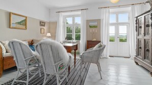Ein Zimmer mit Korbmöbeln, einem Holztisch und Blick ins Freie durch große Fenster.