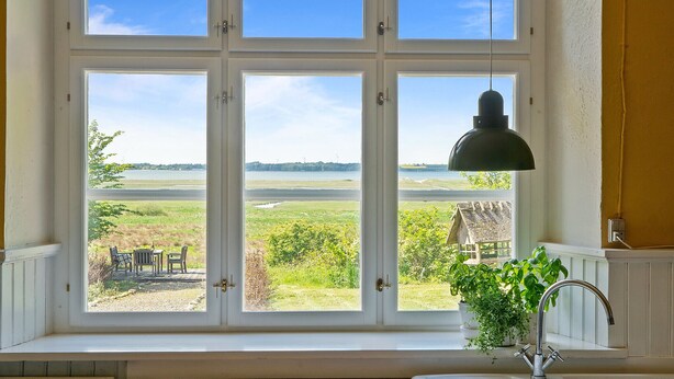 Eine Küche mit großem Fenster mit Blick auf ein grasbewachsenes Feld und ein Gewässer.