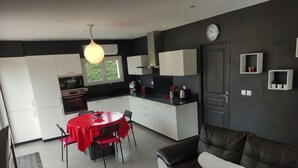 Een moderne keuken met witte kasten, een rode eettafel en een zwarte bank in de woonkamer.
