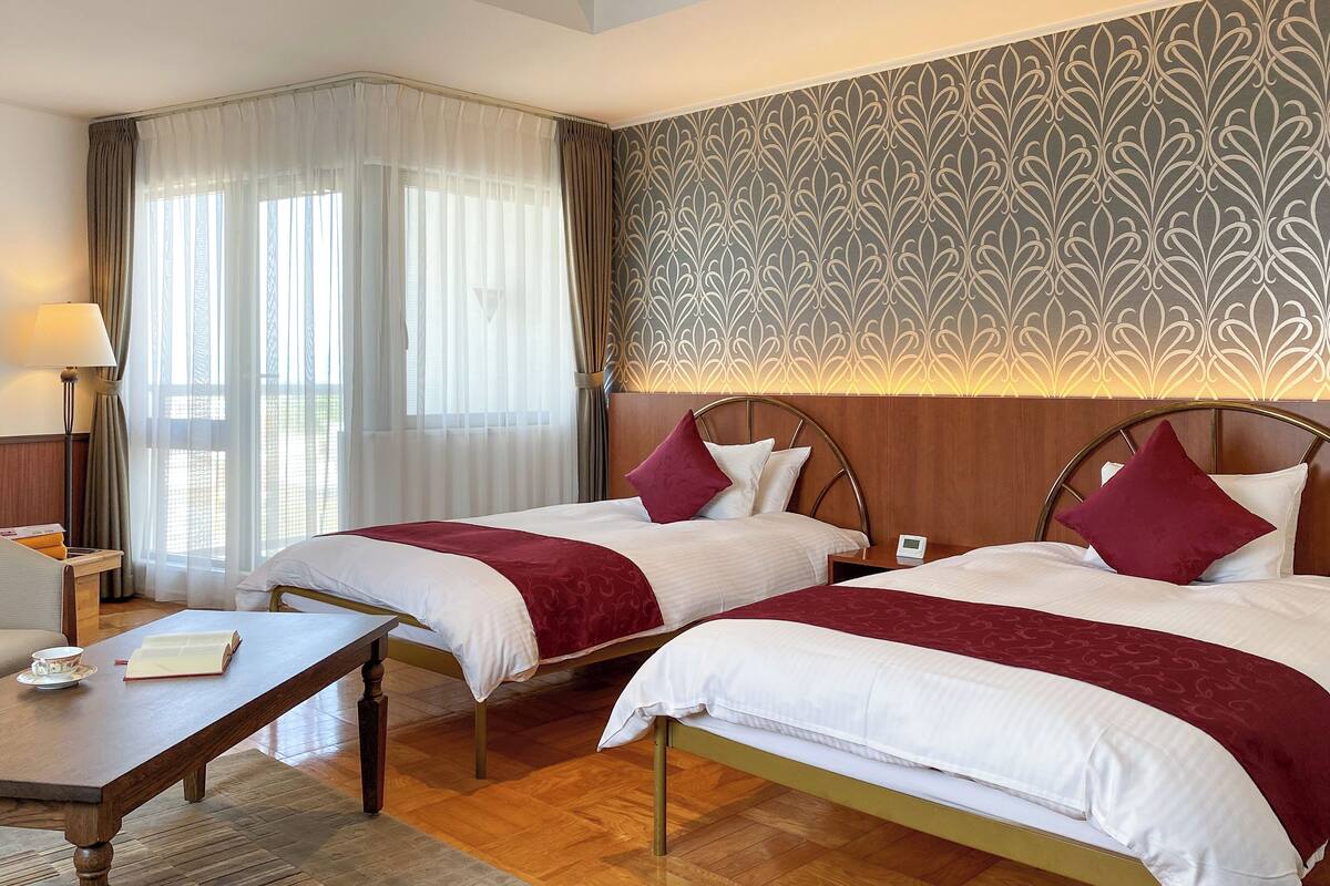Een hotelkamer met twee bedden, een houten tafel, een nachtkastje, een lamp en behang met een patroon.