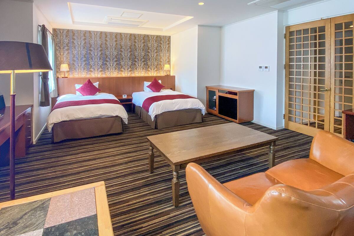 Een hotelkamer met twee bedden, een bureau, een salontafel, een stoel, een kast en een traditionele Japanse schuifdeur.
