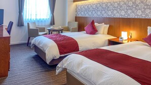 A hotel room with two beds, a desk, a chair, a small table, and a window with curtains. - La Jolie Motomachi (Hakodate)
