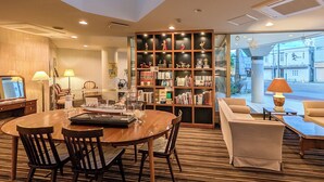 A hotel room with a dining area, a bookshelf, a sofa, and a view of the street. - La Jolie Motomachi (Hakodate)