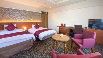 A hotel room with two beds, a desk, a chair, a television, and a patterned carpet.