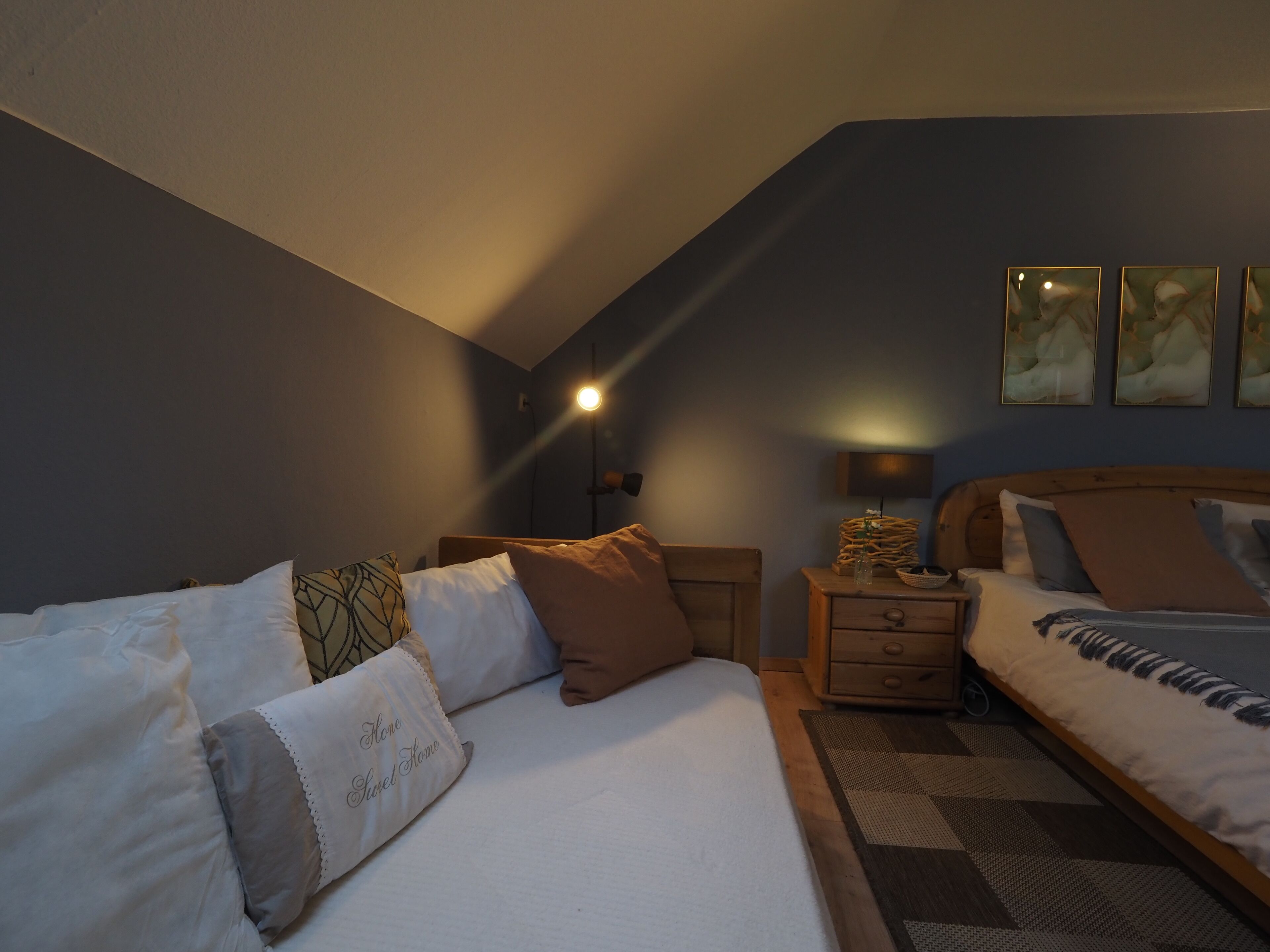 A bedroom with a sloped ceiling, a bed with multiple pillows, a bedside table with a lamp, and a wall-mounted TV.