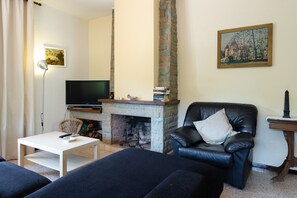 Een woonkamer met een open haard, een televisie, een zwarte leren bank en een witte salontafel.