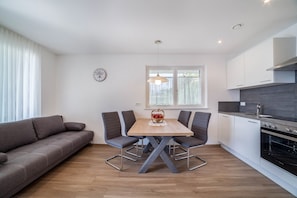 A modern kitchen with white cabinets, a wooden dining table, and a built-in oven.