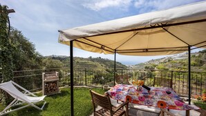 A covered outdoor seating area with a table and chairs, a lounge chair, and a grill.