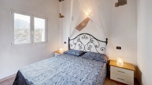 Een slaapkamer met een bed, twee nachtkastjes, een raam en een plafond met een houten balk.