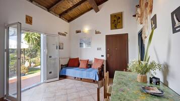 A room with a bed, a table with a floral tablecloth, a door, and a view through a glass door.