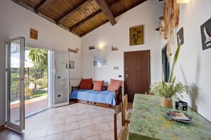 A room with a bed, a table with a floral tablecloth, a door, and a view through a glass door.