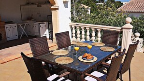 Ein Essbereich im Freien mit Korbstühlen und einem Glastisch, umgeben von einer gefliesten Terrasse.