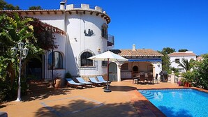 Eine Villa mit Swimmingpool, Sitzgelegenheiten im Freien und einer Terrassenfläche.