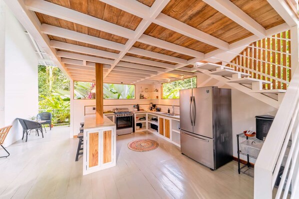A modern kitchen with a central island, stainless steel appliances, and a view of lush greenery outside.