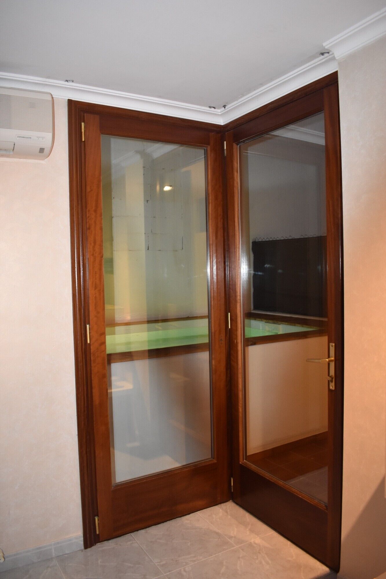 Una habitación de esquina con puerta de madera, piso de baldosas y un respiradero en el techo.