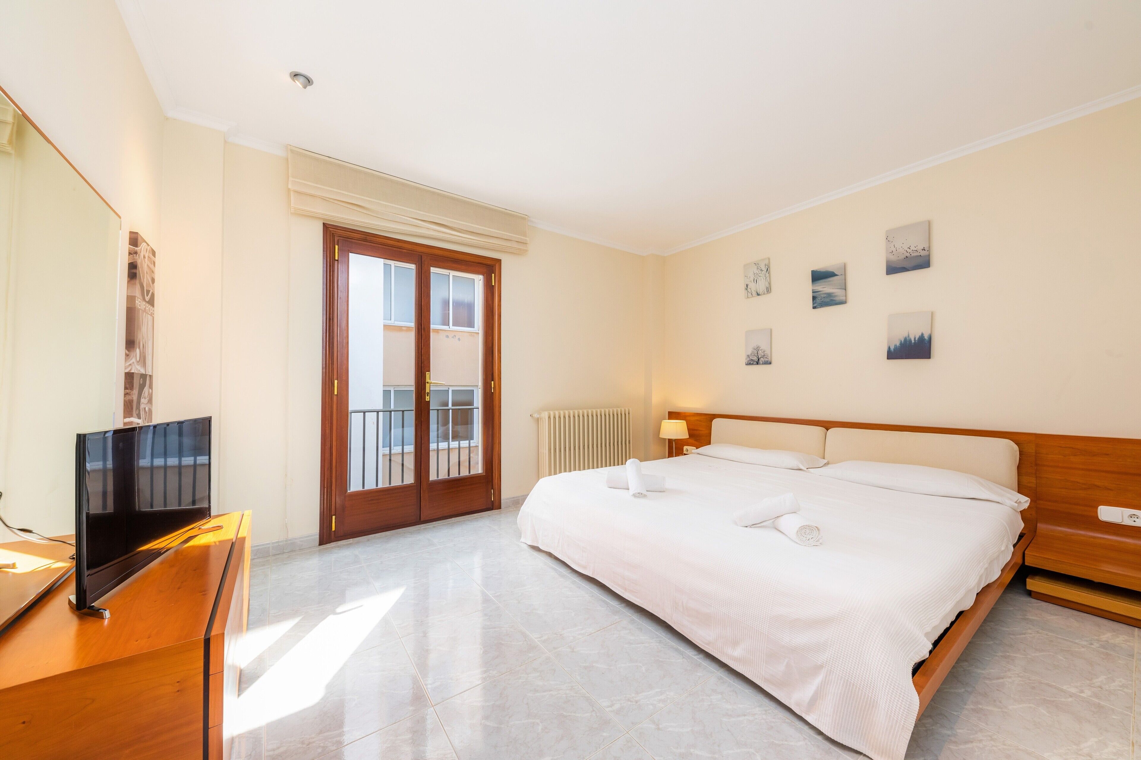 Hotelkamer met een bed, een televisie, een houten dressoir, een balkondeur en wanddecoratie.