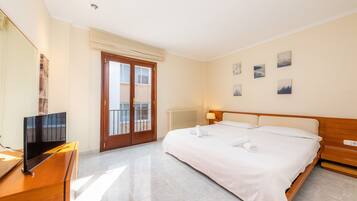 Hotelkamer met een bed, een televisie, een houten dressoir, een balkondeur en wanddecoratie.