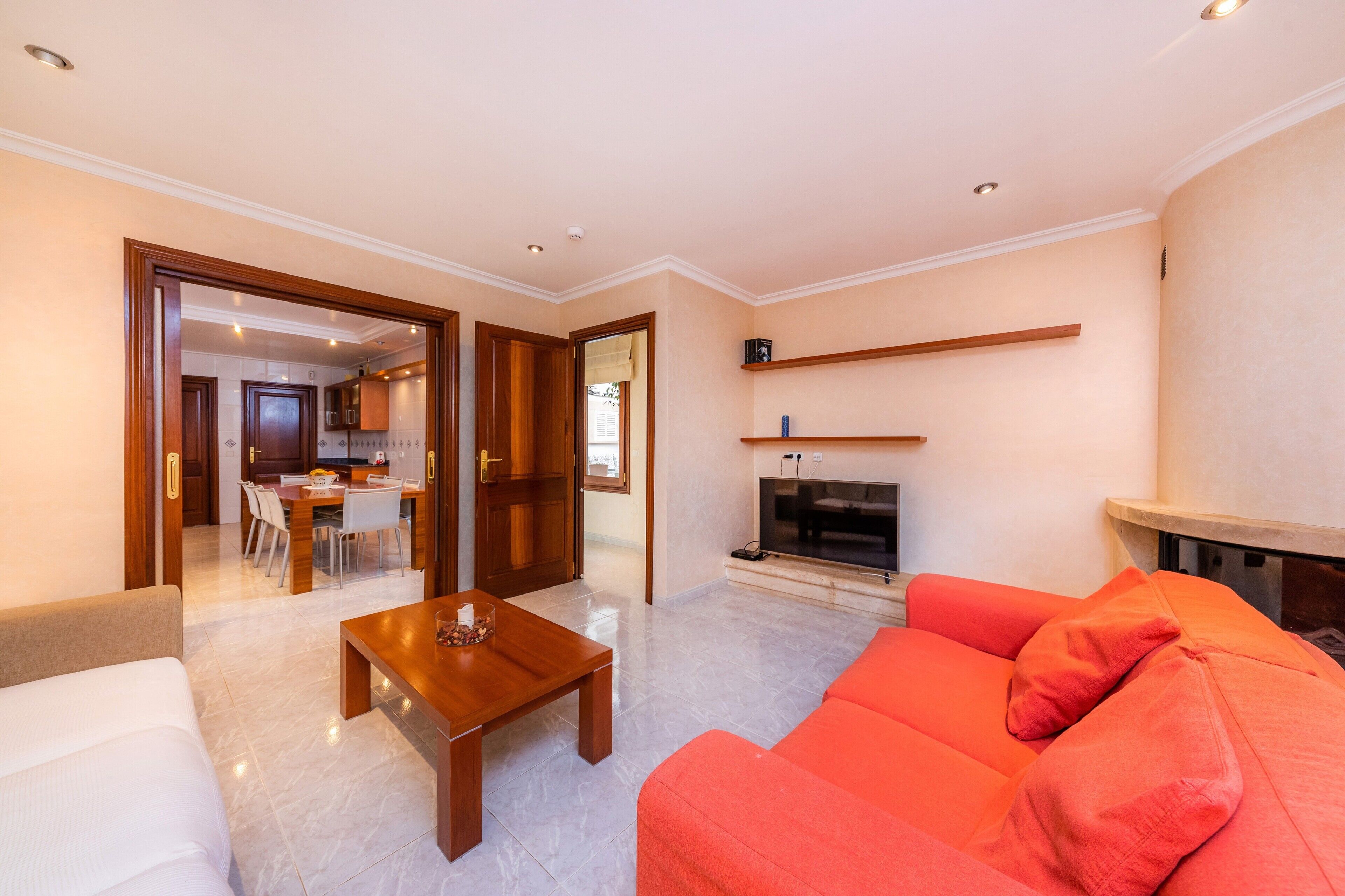 A modern living room with a sofa, a coffee table, a fireplace, and a dining area visible through an open door.