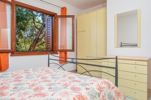 Ein Schlafzimmer mit Bett, Kleiderschrank, Spiegel und einem Fenster mit Blick auf Bäume.