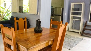 Un coin repas avec une table et des chaises en bois, un vase, et une cuisine visible à travers une porte ouverte.