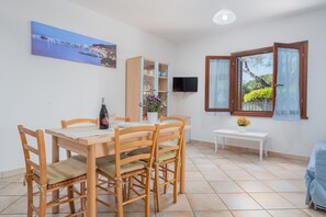 A dining area with a wooden table and chairs, a cabinet with glass doors, a flat-screen TV mounted on the wall, and a window with curtains.