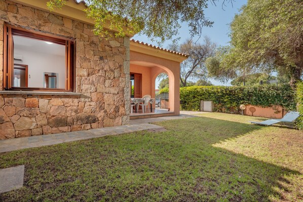 A stone house with a patio, a lawn, and a tree.
