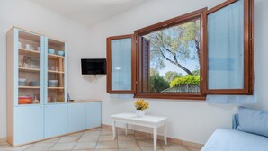 Une pièce avec un lit, une petite table ornée d’un vase de fleurs, un buffet contenant de la vaisselle et un téléviseur fixé au mur.