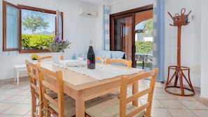 Un coin repas avec une table en bois, des chaises, une bouteille de vin et un vase de fleurs.