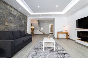 A modern living room with a stone wall, a sofa, a coffee table, a TV, and a staircase leading to another room.
