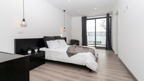 Een moderne slaapkamer met een bed, nachtkastjes, een dressoir en een groot raam met gordijnen.