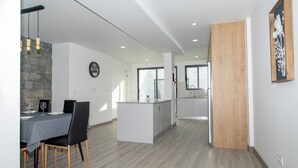 Een moderne keuken met een centraal eiland, een eethoek met een tafel en stoelen, en een wand met stenen details.