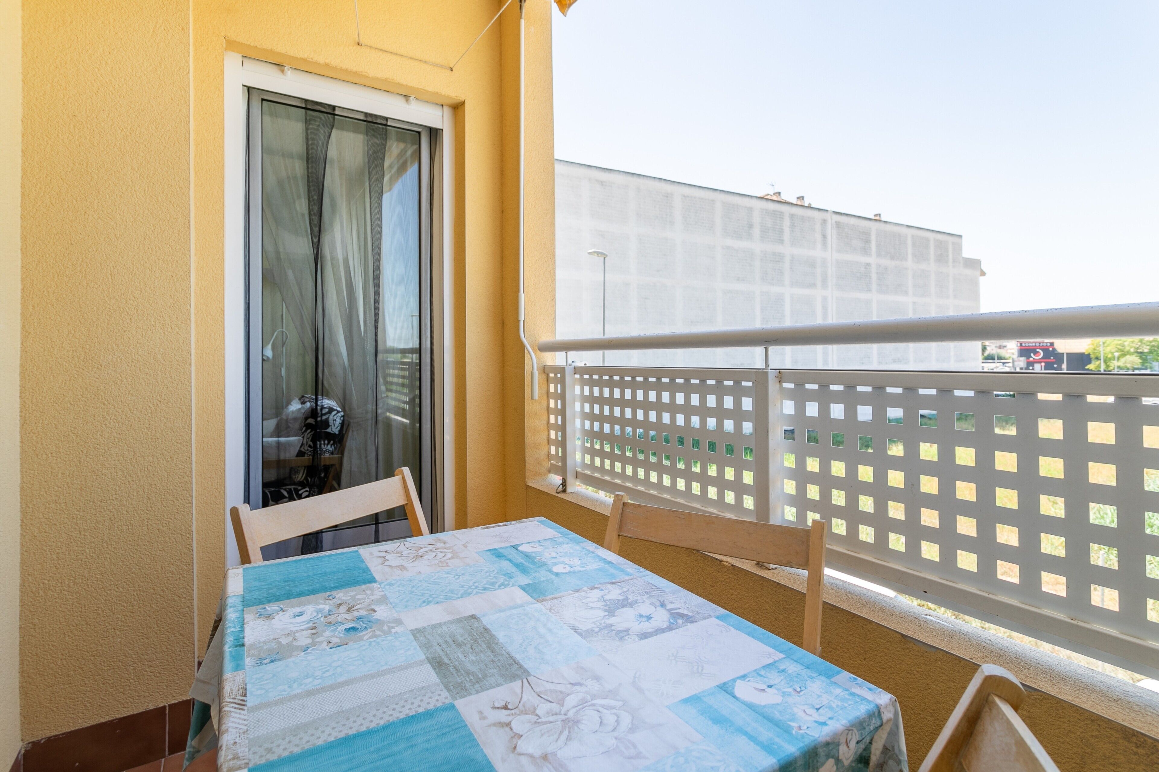 Ein Balkon mit Tisch und Stühlen, einem weißen Gittergeländer und einem Gebäude im Hintergrund.