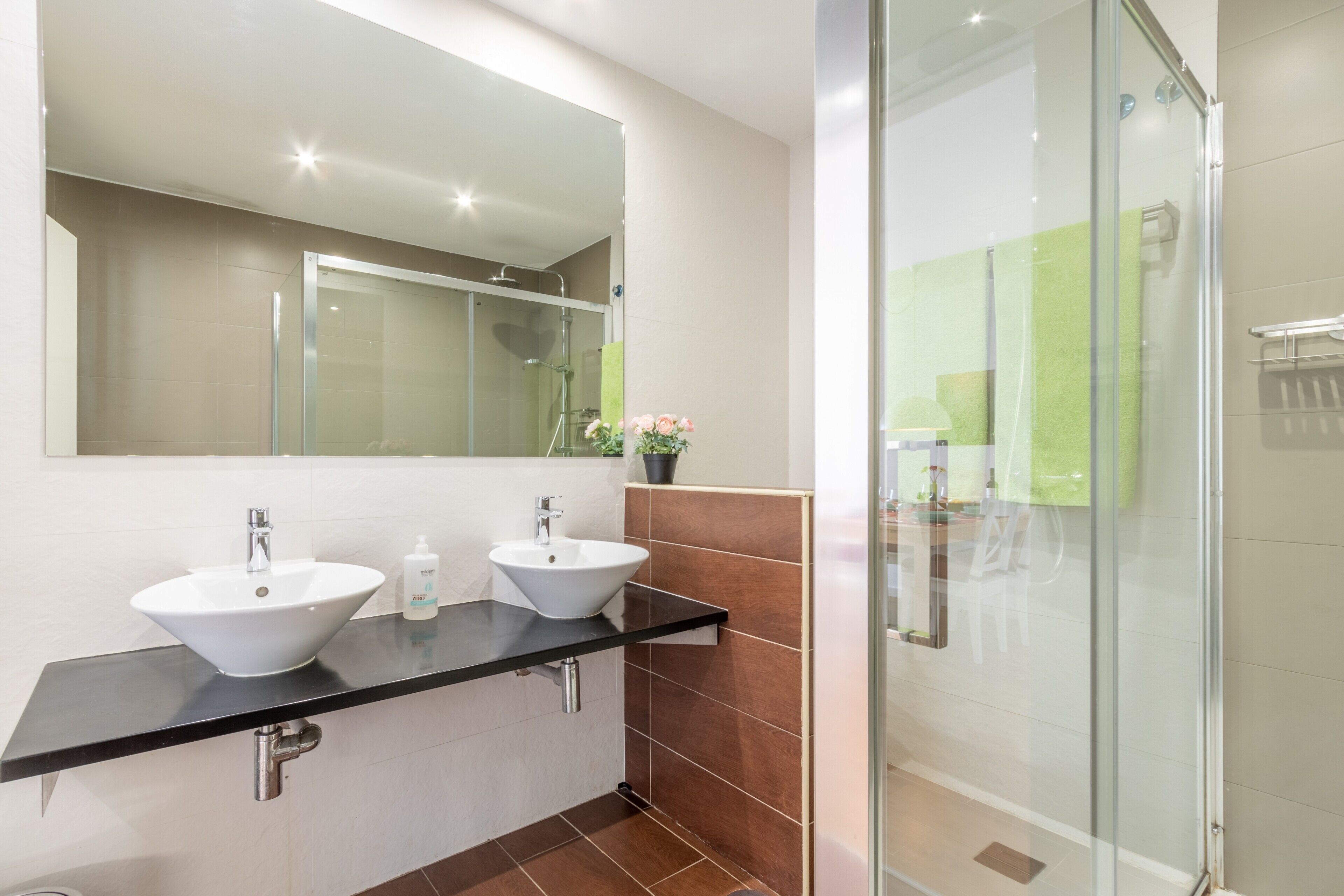 A modern bathroom with two sinks, a large mirror, and a glass shower enclosure.