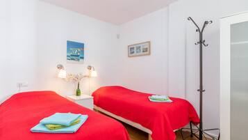 A room with two beds, a nightstand with a lamp, a picture on the wall, and a coat rack.