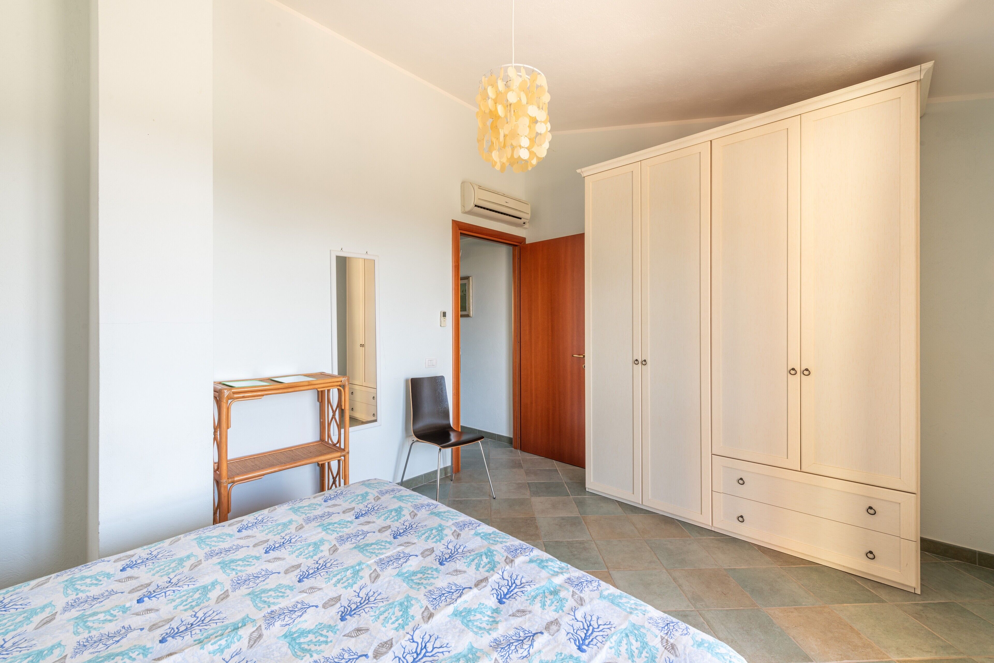 Ein Schlafzimmer mit Bett, Kleiderschrank, Stuhl, Schreibtisch und einer Pendelleuchte.