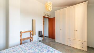 Ein Schlafzimmer mit Bett, Kleiderschrank, Stuhl, Schreibtisch und einer Pendelleuchte.