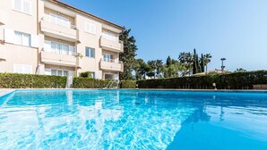 A swimming pool with clear blue water, surrounded by a building with balconies and a hedge. - Apartment 'Xiprer' with Terrace, Shared Pool & Wi-Fi (PORT POLLENÇA)