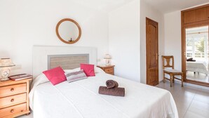 A bedroom with a bed, a wooden nightstand, a mirror, a chair, and a door leading to a balcony. - Apartment 'Xiprer' with Terrace, Shared Pool & Wi-Fi (PORT POLLENÇA)