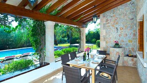 Un patio al aire libre con una mesa y sillas, un muro de piedra y vistas a una piscina.