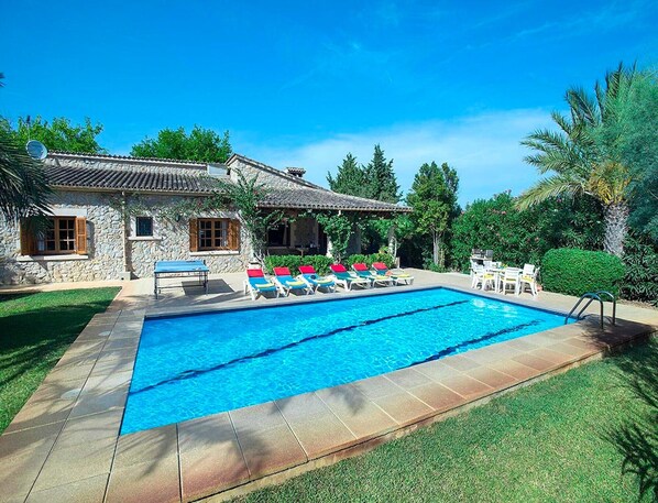 A swimming pool with lounge chairs, a stone building, and a well-maintained lawn.
